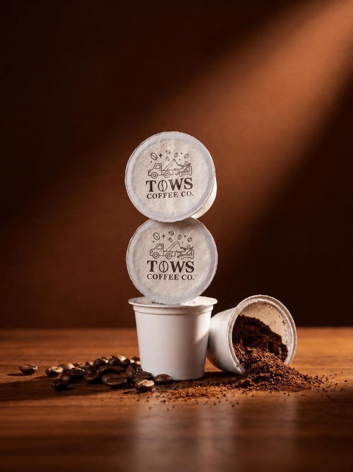 Three TOWS Coffee Co. coffee pods on a wooden surface with coffee beans and grounds.