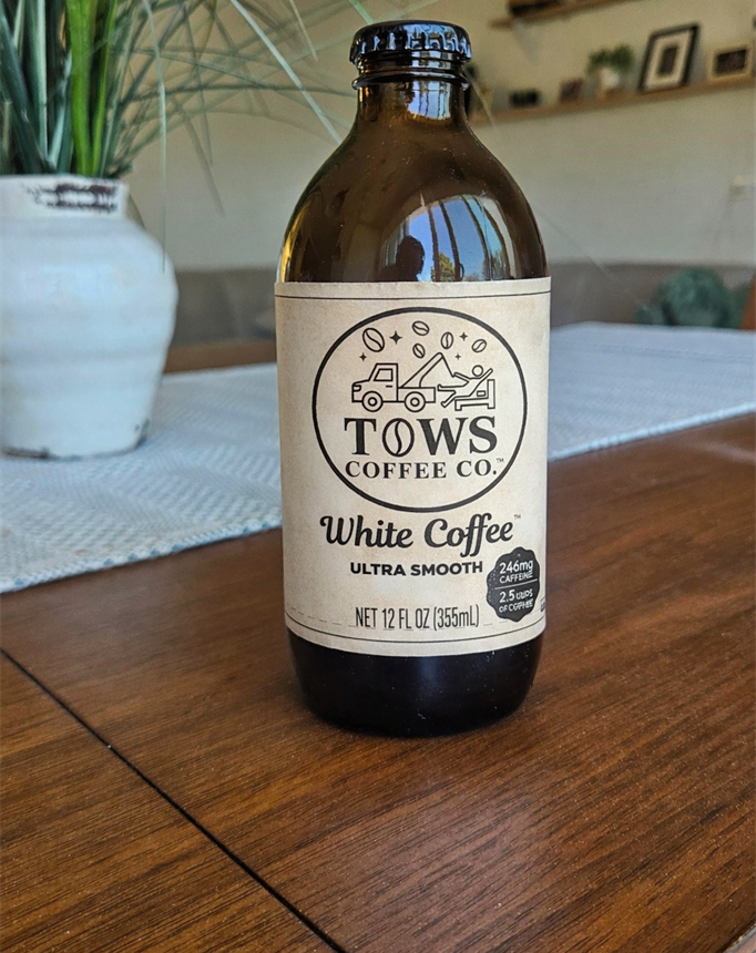 Bottle of TOWS Coffee Co. White Coffee on a wooden table with a homey background.